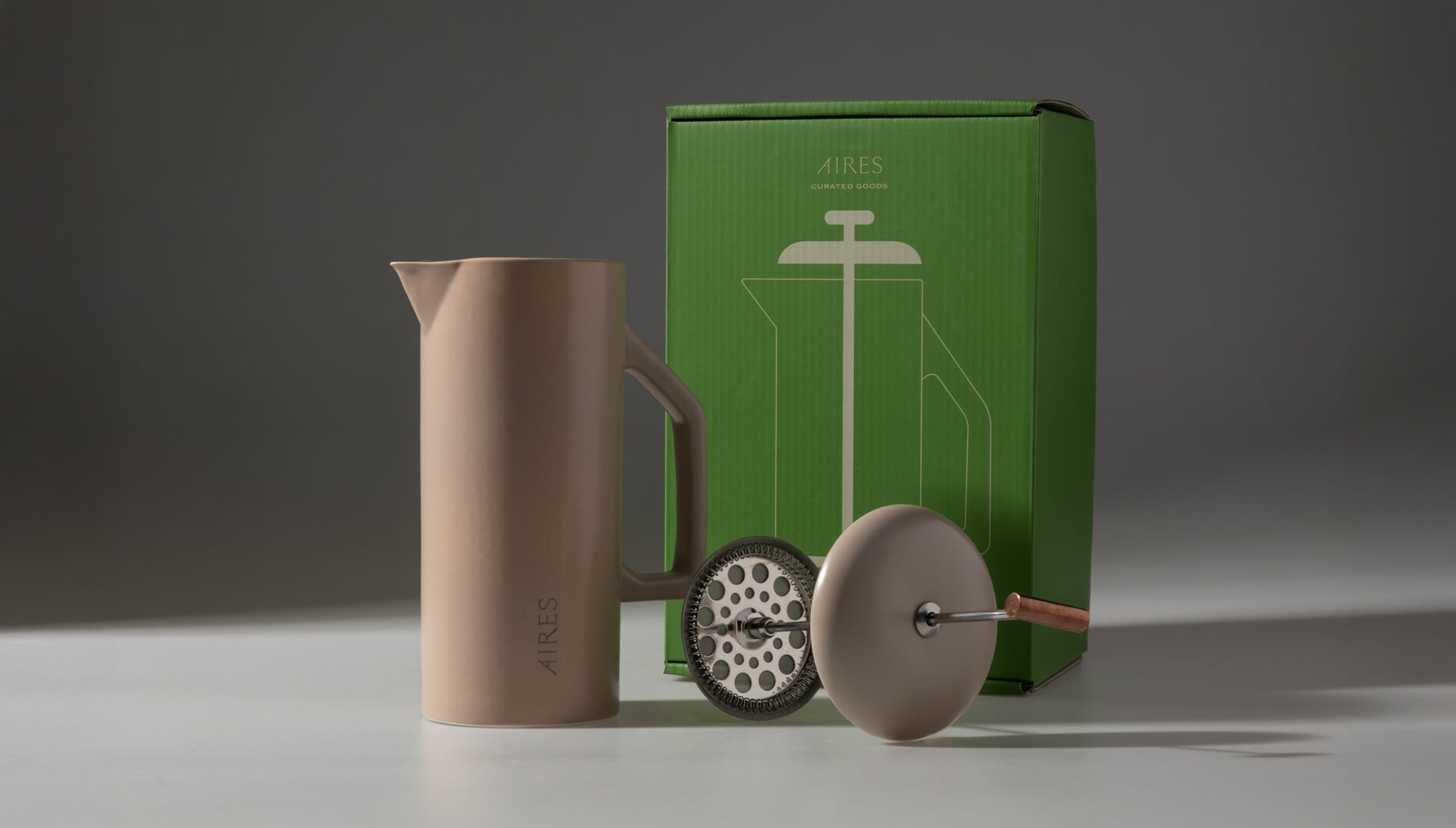 AIRES ceramic French press in taupe with stainless steel filter and green packaging box featuring a minimalist line illustration.